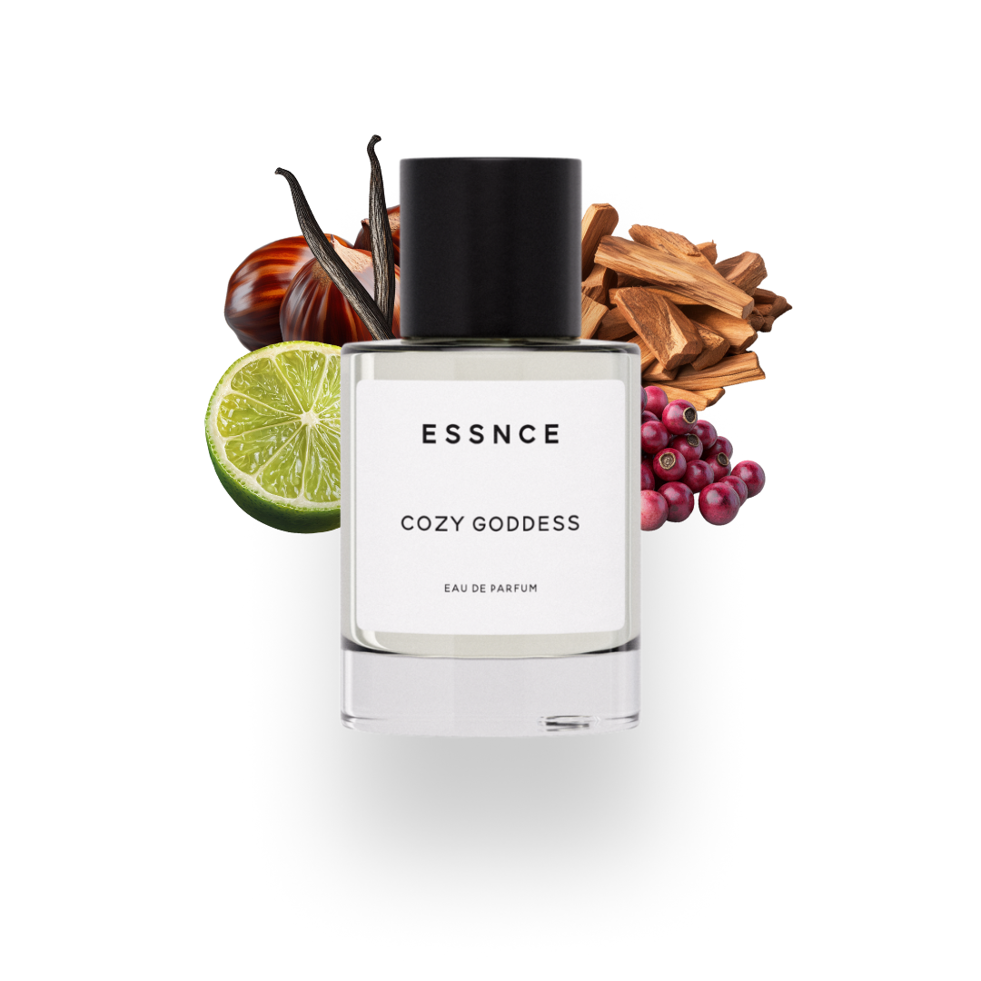 En flaska ESSNCE Cozy goddess Eau de Parfum visas med en svart kork och en vit etikett. Bakom flaskan finns ingredienser som rosepeppar, kastanj, sandelträ, bergamott och vanilj.