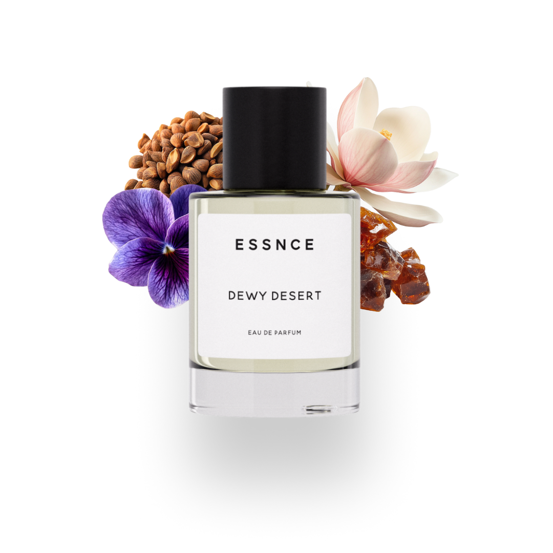 En flaska ESSNCE Dewy Desert Eau de Parfum visas med en svart kork och en vit etikett. Bakom flaskan finns ingredienser som Magnolia, ambrette seeds, amber och viol.