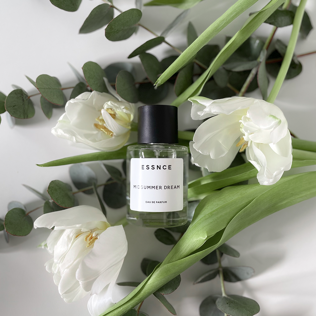 En flaska ESSNCE Midsummer dream Eau de Parfum som ligger ovanpå några blommor med stjälk.