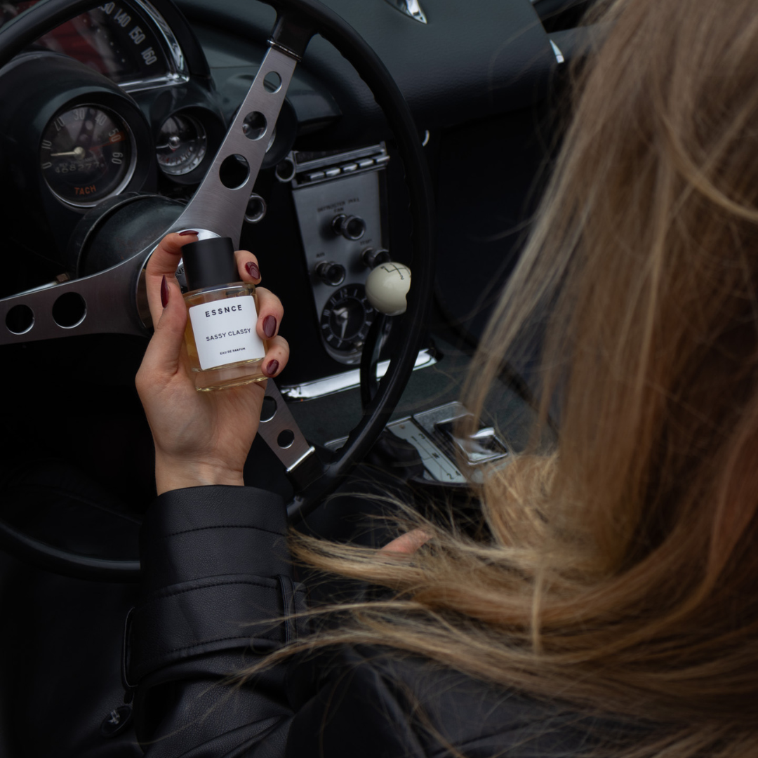 A person with long blonde hair holds a bottle of perfume labeled 